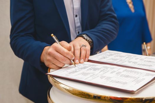 Groom's man's hands put on the signature in the magazine about consent to marriage at the wedding.