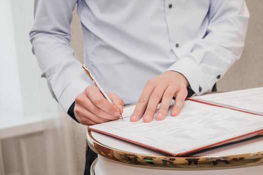 The hands of the witness's boyfriend in the shirt put the signature on the wedding close-up.