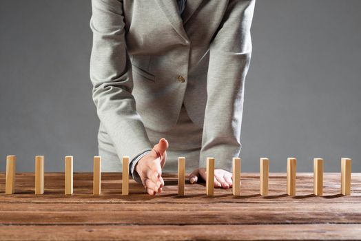 Close up female hand interrupting domino effect. Operative business solution, strategy and successful intervention. Business assistance concept with wooden blocks. Protection from economic crisis.