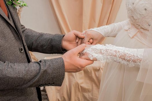 Male groom's hands hold bride's hands in wedding gloves.