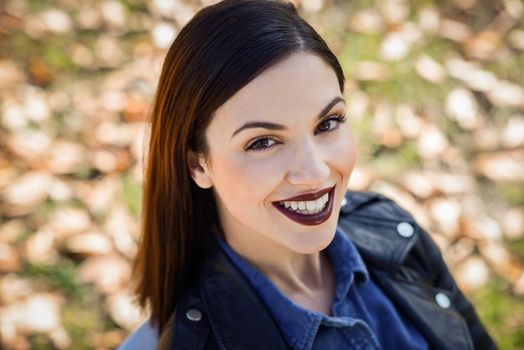 Beautiful young woman, smiling in urban background. Girl wearing leather jacket and blue shirt