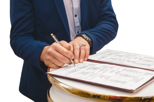 Groom's man's hands put on the signature in the magazine about consent to marriage at the wedding.