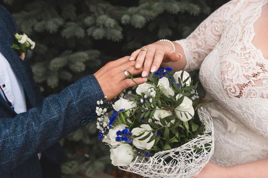 The bride and groom put their hands on the wedding bouquet of flowers of white roses, close-up of tenderness and romance.