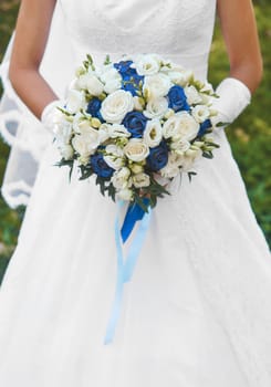 Bride in white wedding dress holds a bouquet of flowers white and blue roses close up.