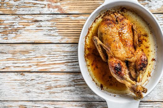 Baked whole farm duck in a baking dish. White wooden background. Top view. Space for text.