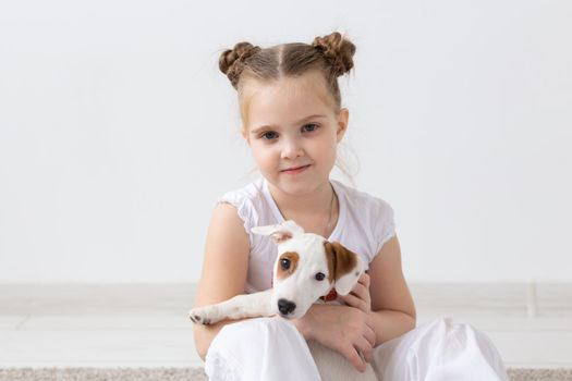 People, pets and animal concept - Little girl sitting on the floor over white background and holding puppy Jack Russell Terrier.