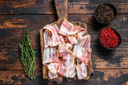 Raw pork bacon meat slices on a wooden cutting board. Dark wooden background. Top view.