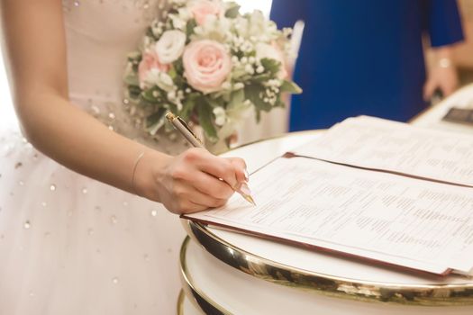 The hand of a young girl bride puts a signature on consent to marriage in the document in the registry office.