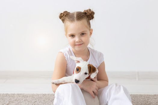 People, pets and animal concept - Little girl sitting on the floor over white background and holding puppy Jack Russell Terrier.