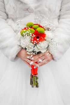 Bride in white coat and wedding dress holds a bouquet of flowers.