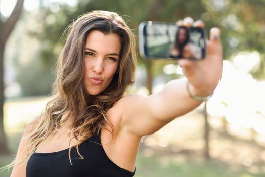 Portrait of a beautiful young woman selfie in the park with a smartphone