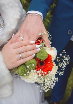 Bride in white coat put her hand on the hand of the groom on the wedding bouquet of flowers, close-up.