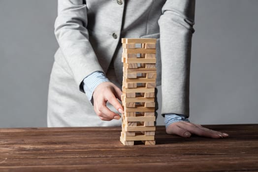 Businesswoman removing wooden block from tower on table. Management of risks concept with wooden boxes game. Business development and assistance. New challenge and leadership motivation.