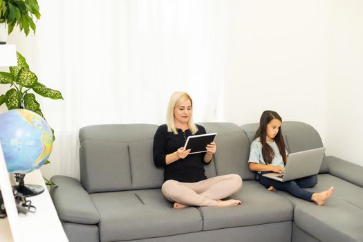 mother works on tablet online and daughter doing homework with a tablet