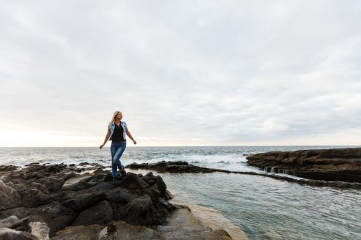 Women on volcanic rocks and blue ocean with waves, white foam and volcanic rocks. Canary Islands. The magnificent coast of the Atlantic Ocean.