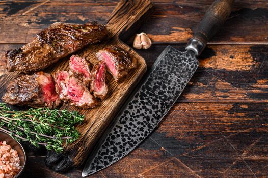 Grilled bbq skirt steaks slices on a wooden board. Dark wooden background. Top view. Copy space.