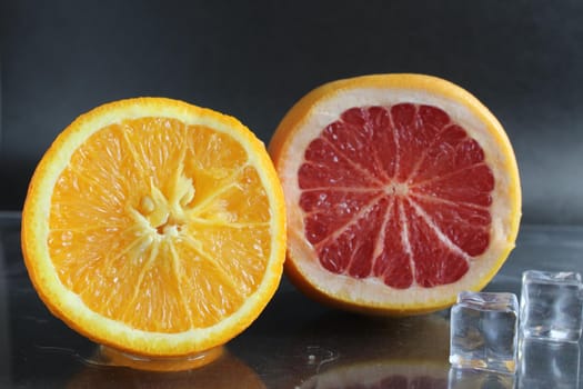 orange and grapefruit in the cut lie next to ice cubes on a black background. Fruit for lemonade. citrus.