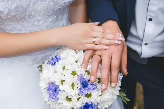 Tenderness and weasel hands of the bride and groom on the wedding bouquet of flowers.