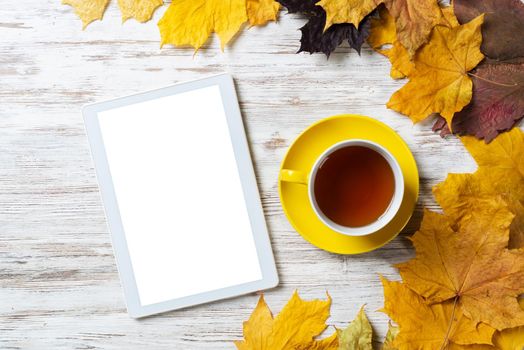 Tablet computer and cup of black tea lies on vintage wooden desk with bright foliage. Flat lay composition with autumn leaves on white wooden surface. Internet communication and digital technology