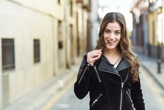 Portrait of young woman smiling in urban background wearing casual clothes with modern sunglasses. Girl with long curly hair