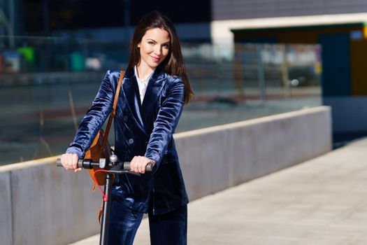 Young business woman wearing blue suit using electric scooter. Lifestyle concept.