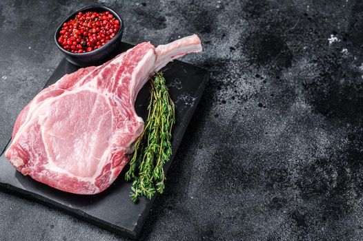 Raw fresh tomahawk pork chop steak on a marble board. Black background. Top view. Copy space.