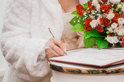 Bride's hand puts signature pen on consent marriage at wedding close-up.