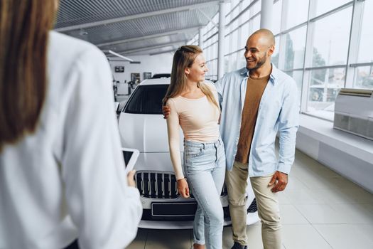 Car saleswoman in a car dealership having a talk with clients buyers