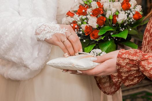 The bride's hand in the wedding glove takes the marriage ring. Close-up of wedding rings.