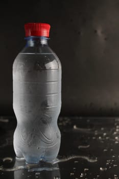 Cold water in a bottle on a black background. A bottle of water stands on a black background. Cool summer drinks.