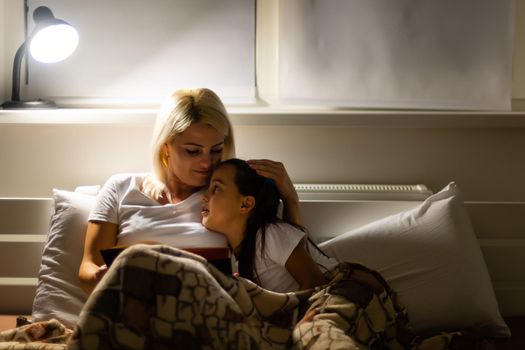 happy family mother and daughter read a book in the evening at home