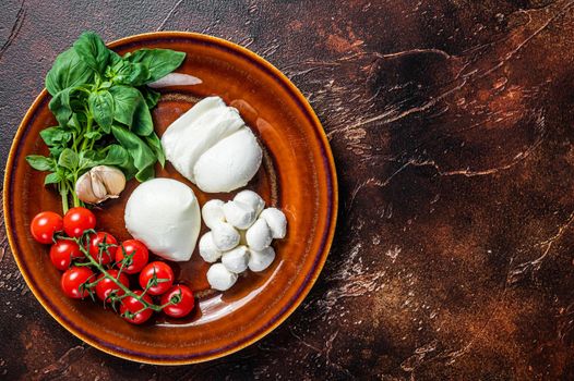 Mozzarella cheese, basil and tomato cherry ready for cooking Caprese salad. Dark background. Top view. Copy space.