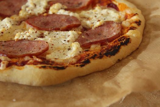 homemade pizza with ham and cheese lies on parchment close-up view super on the side. Homemade fast food background.