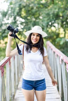 Beautiful hiker young woman taking photographs with a mirrorless camera, wearing straw hat, hiking in the countryside.