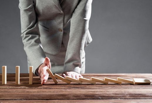 Close up female hand interrupting domino effect. Operative business solution, strategy and successful intervention. Business assistance concept with wooden blocks. Protection from economic crisis.