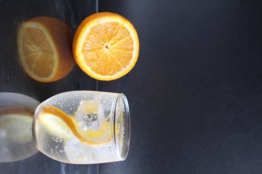 lemonade with orange and ice in a glass on a black background next to lies ice and orange. Summer drink on a black background.