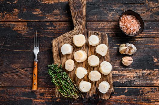 Steamed scallops meat on a wooden board. Dark wooden background. Top view.