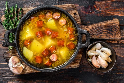 Split pea soup with smoked sausages in a pan. Dark wooden background. Top view.