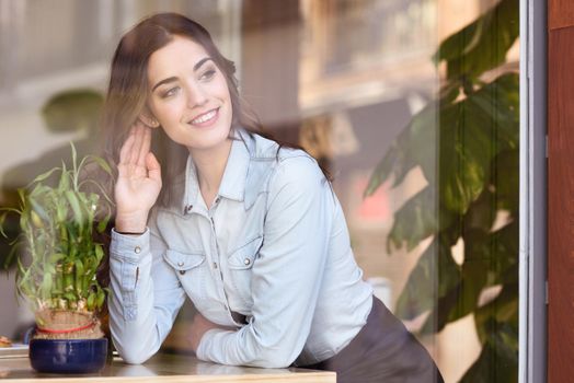 Cafe city lifestyle. Young woman sitting indoor in trendy urban cafe looking through the window. Cool young modern caucasian female model in her 20s