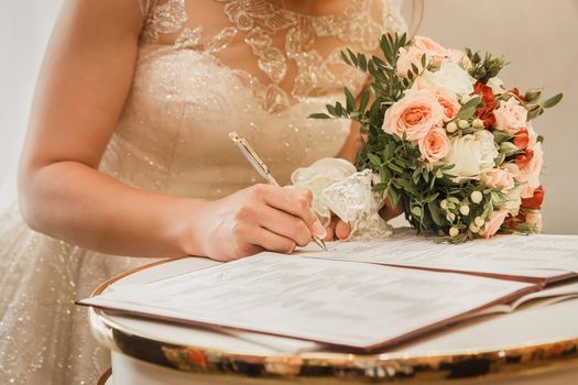 Bride's hand puts signature pen on consent to marry at wedding close-up.