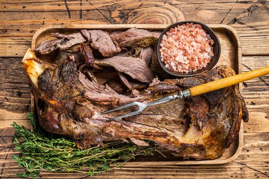 Roasted lamb mutton cutting shoulder meat in a wooden tray with meat fork. wooden background. Top view.