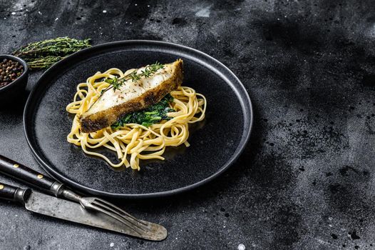 Spaghetti pasta with Halibut fish steak and spinach. Black background. Top view. Copy space.