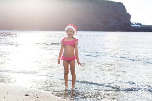 Little cute girl in red hat santa claus on the beach
