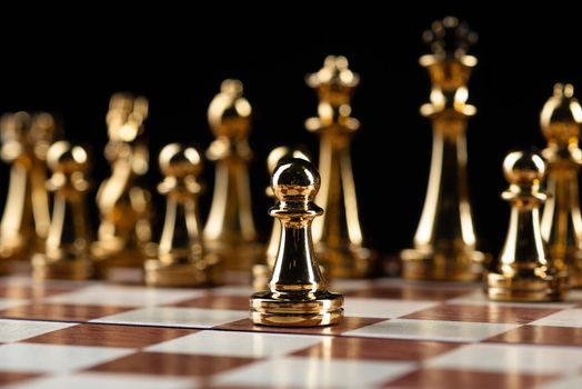 Golden chess figures standing on wooden chessboard. Intellectual duel and tactical battle in business. Strategy planning and leadership concept. Gold metal chess pieces in row on black background.
