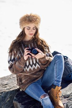 Young woman taking photographs in the snowy mountains in winter, in Sierra Nevada, Granada, Spain. Female wearing winter clothes.