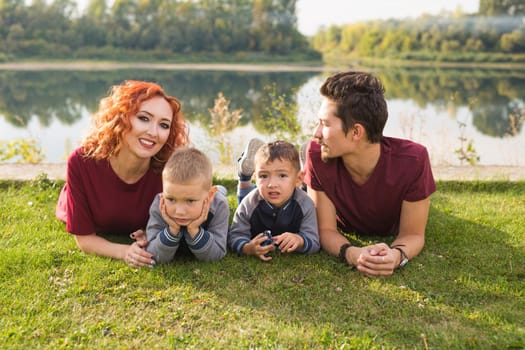 Parenthood, nature, people concept - family with two sons sitting near the lake.