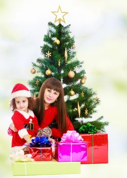 Beautiful mother and daughter , dressed in the costume of Santa Claus around the Christmas tree surrounded by heaps of gifts.white-green blurred abstract background with snowflakes.