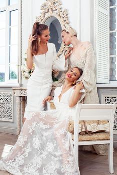 three young pretty lady in white lace fashion style dress posing in rich interior of royal hotel room, luxury lifestyle people concept, bride on wedding day closeup