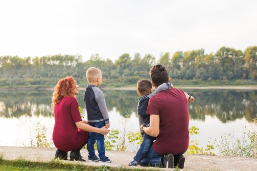 Parenthood, childhood and family concept - Parents and two male children walking at the park and looking on something.