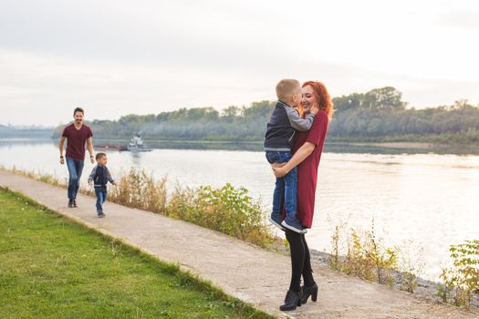 Family and children concept - mother, father and two sons enjoying the summer time, playing near the river.